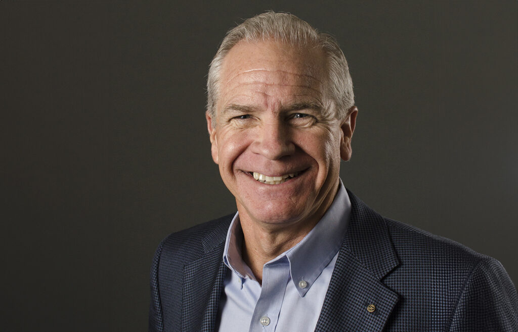 Patrick Mullen smiling in a navy blue blazer and light blue shirt against a dark background