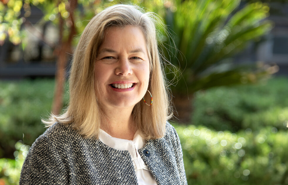 Professional headshot of Andrea Burns smiling outdoors with greenery in the background