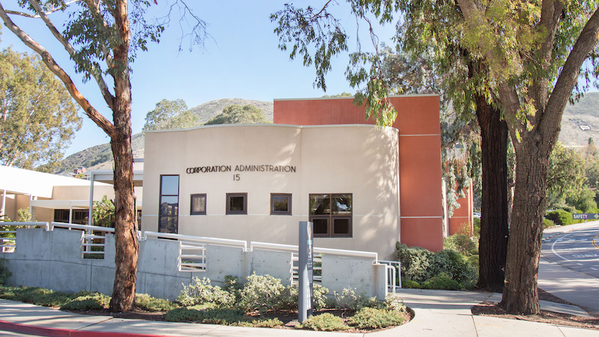 Exterior view of the Corporation Administration building at Cal Poly, labeled Building 15, surrounded by trees and landscaping on a sunny day.