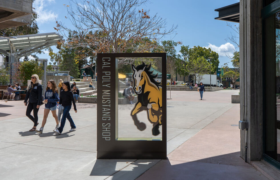 Students walking on Cal Poly’s campus near the Mustang Shop sign with a horse logo