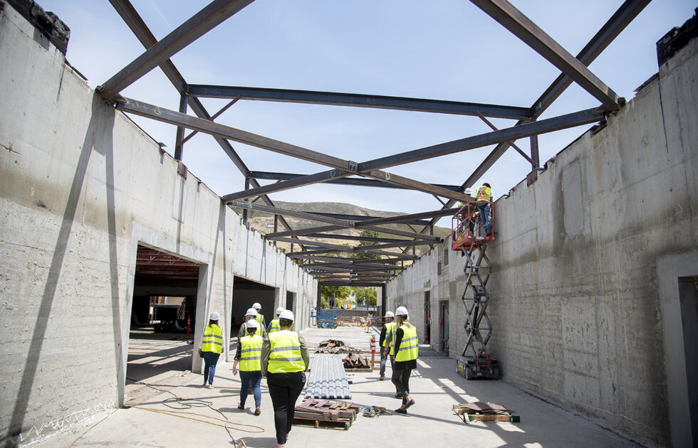 Construction crew in yellow safety vests walking through a concrete-framed building under steel beams