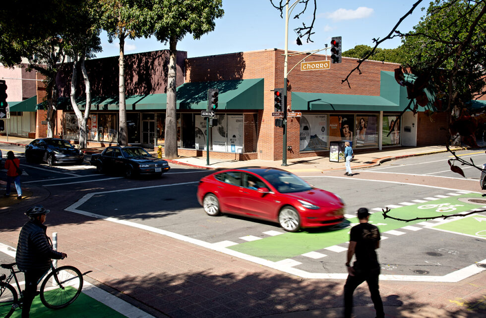Busy street corner in downtown San Luis Obispo with a red car driving through the intersection at Chorro and Higuera streets