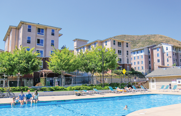 Students relaxing at the pool at Poly Canyon Village student housing on a bright, sunny day