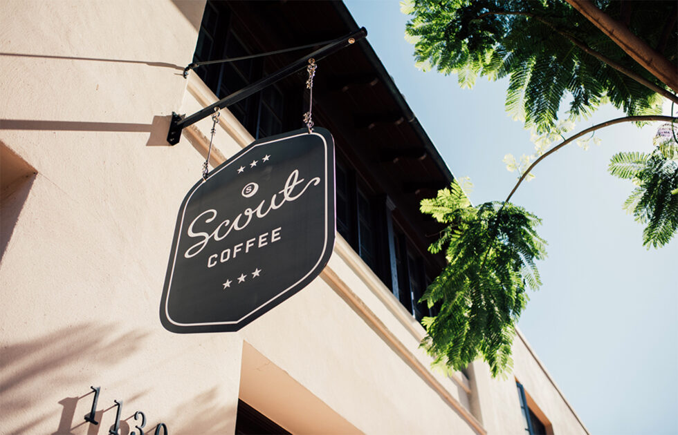 Sign for Scout Coffee hanging outside a downtown San Luis Obispo location with trees and a sunny sky
