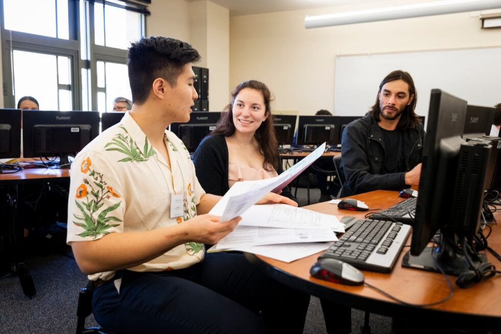 Students discussing paperwork during a computer lab group project