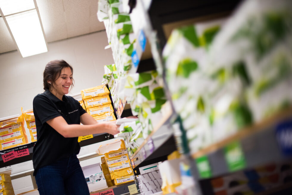 Young woman organizing paper supplies on shelves in a print or supply room