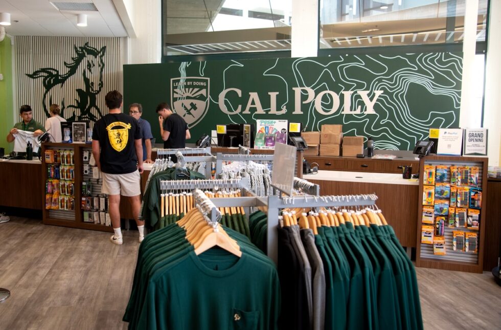 Interior of Cal Poly campus store with merchandise, students, and a green feature wall.