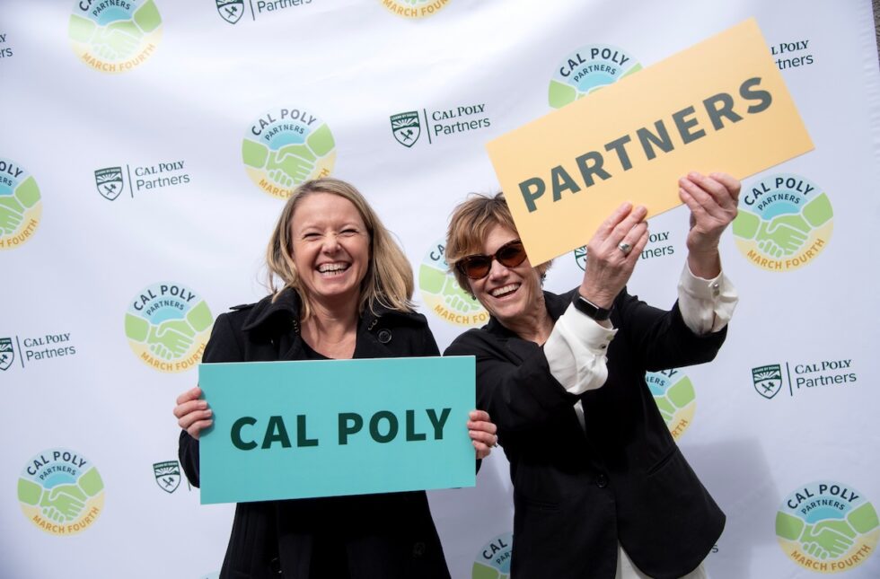 Two women holding “Cal Poly” and “Partners” signs at a Cal Poly Partners March Fourth event.