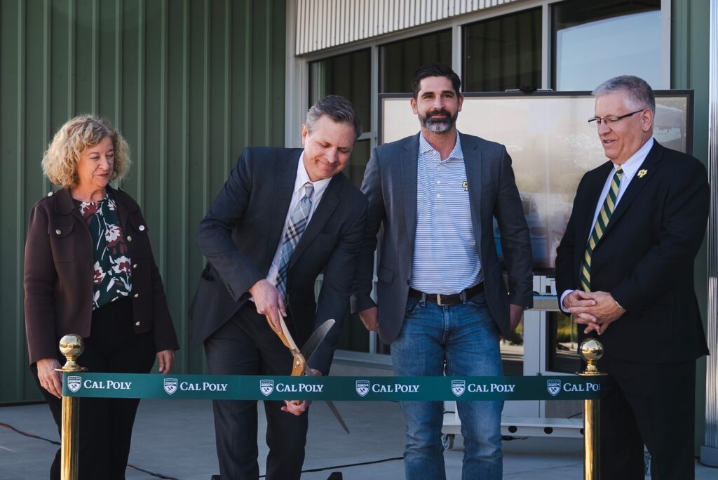 A man cuts a Cal Poly ribbon as three attendees look on during an outdoor ceremony.