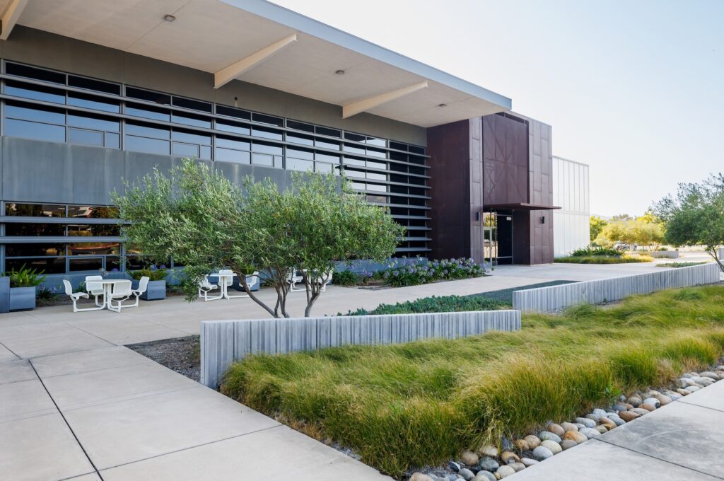 A modern office building features shaded windows, landscaped walkways and outdoor seating.