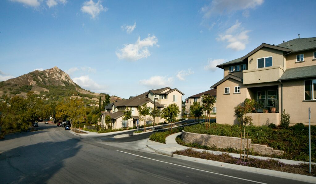 Homes line a landscaped residential street with a rocky mountain in the background.